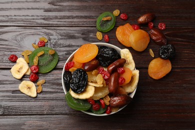 Photo of Mix of different dried fruits in bowl on wooden table, flat lay