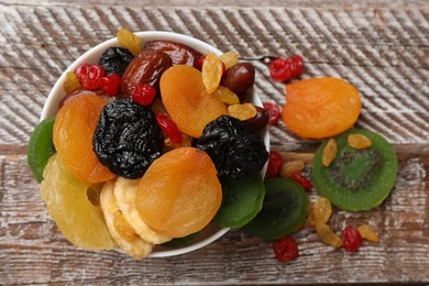 Photo of Mix of different dried fruits in bowl on wooden table, top view