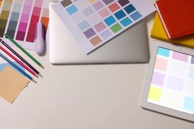 Photo of Designer's workplace with tablet, laptop, palettes and stationery on white table, flat lay