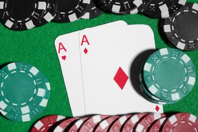 Photo of Playing cards and poker chips on green table, flat lay