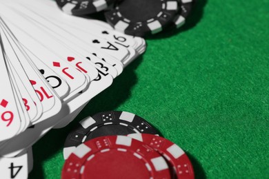 Photo of Playing cards and poker chips on green table, closeup. Space for text