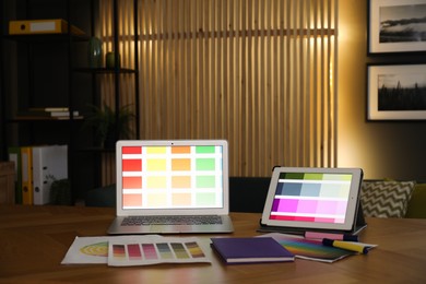 Photo of Designer's workplace with laptop, tablet, stationery and palettes on wooden table indoors