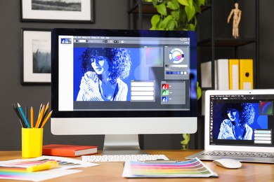 Photo of Designer's workplace with computer, laptop, stationery and palettes on wooden table indoors