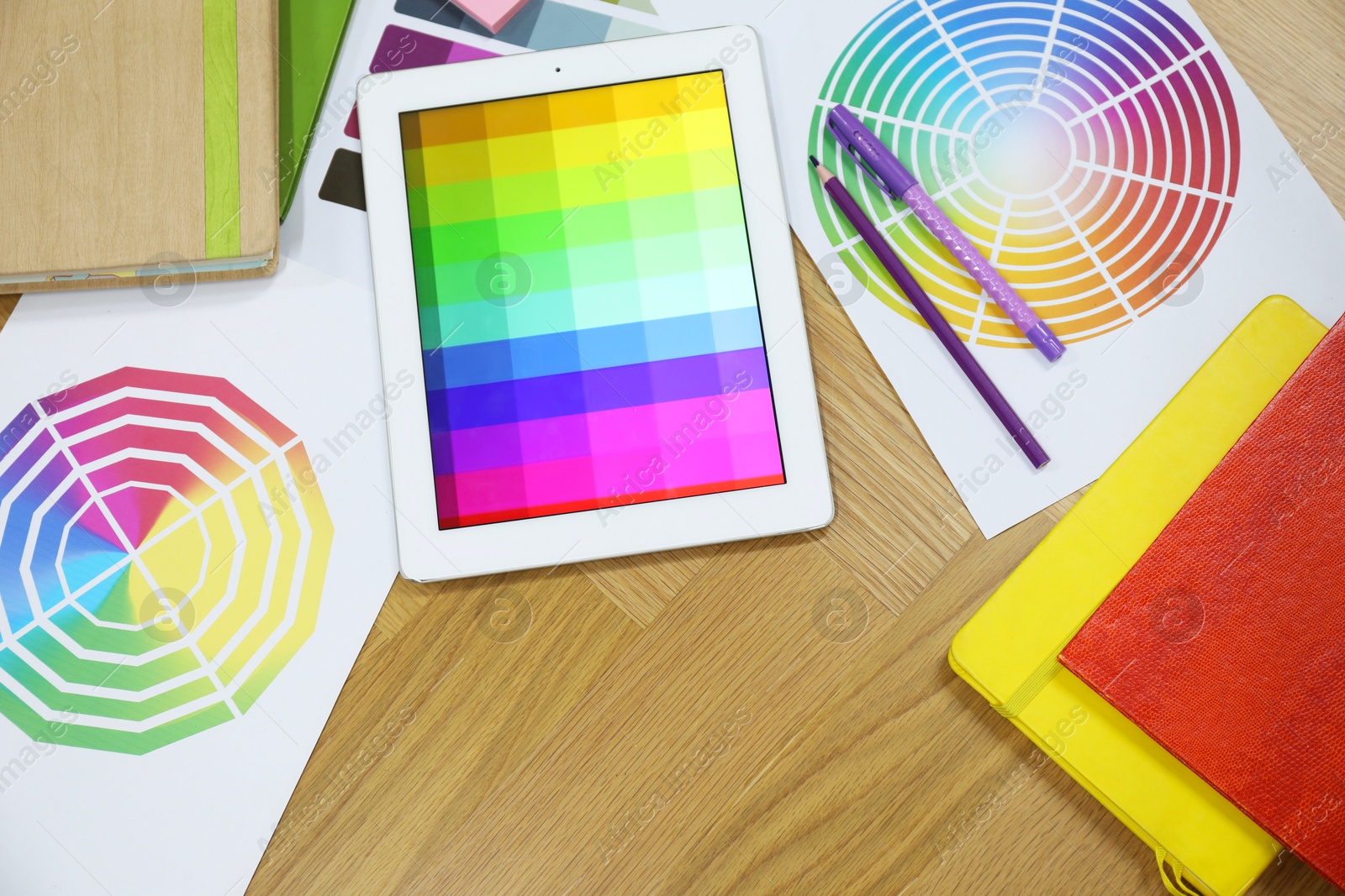 Photo of Designer's workplace with tablet, palettes and stationery on wooden table, flat lay