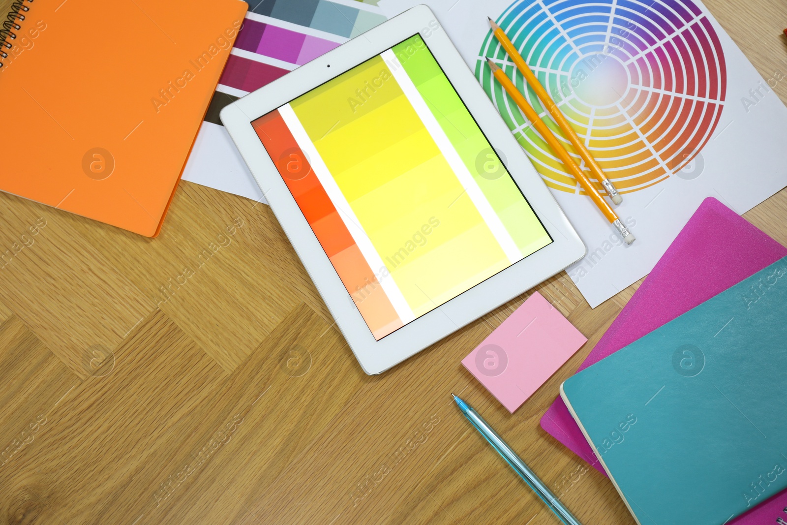 Photo of Designer's workplace with tablet, palettes and stationery on wooden table, flat lay