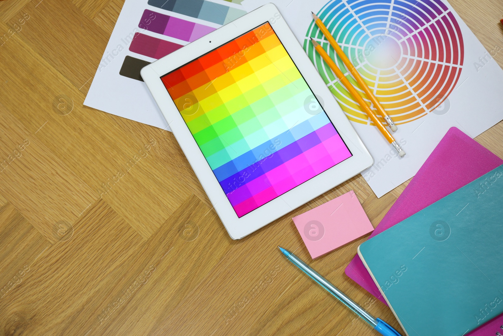 Photo of Designer's workplace with tablet, palettes and stationery on wooden table, flat lay