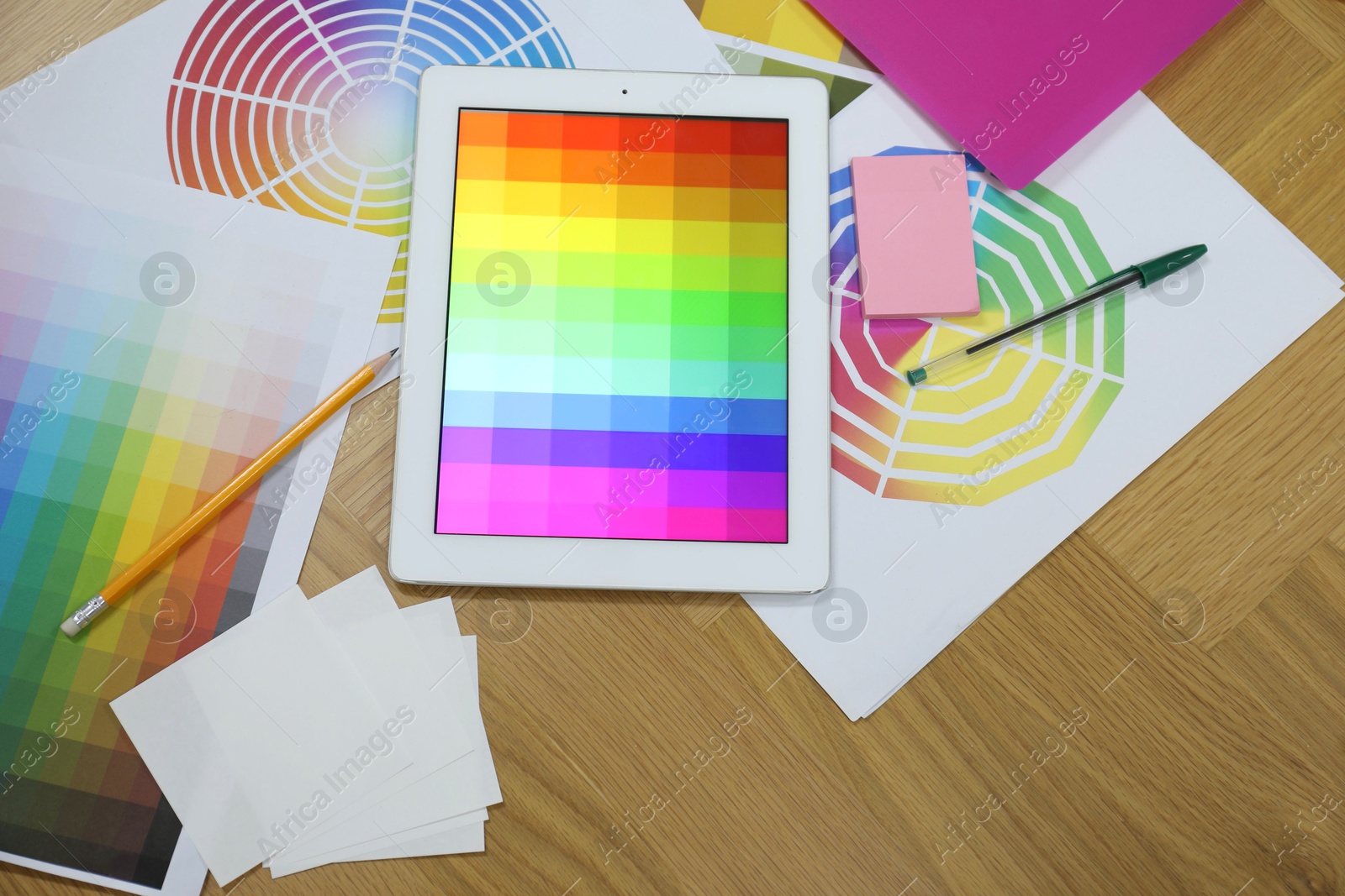 Photo of Designer's workplace with tablet, palettes and stationery on wooden table, flat lay