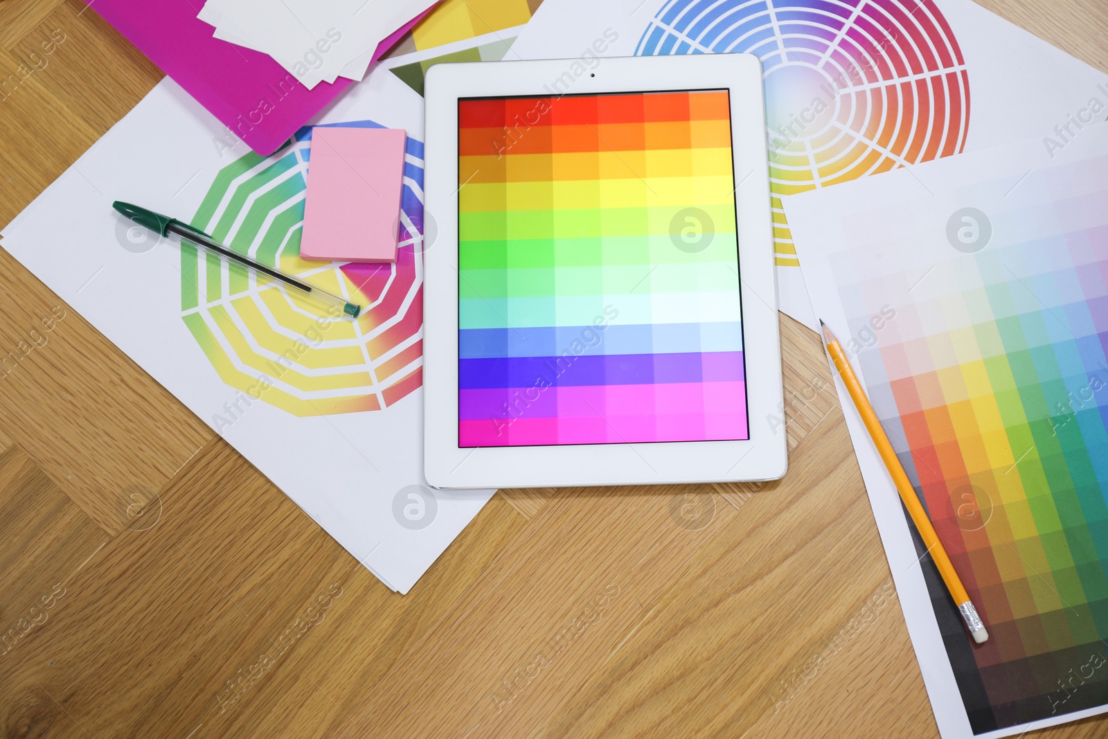 Photo of Designer's workplace with tablet, palettes and stationery on wooden table, flat lay