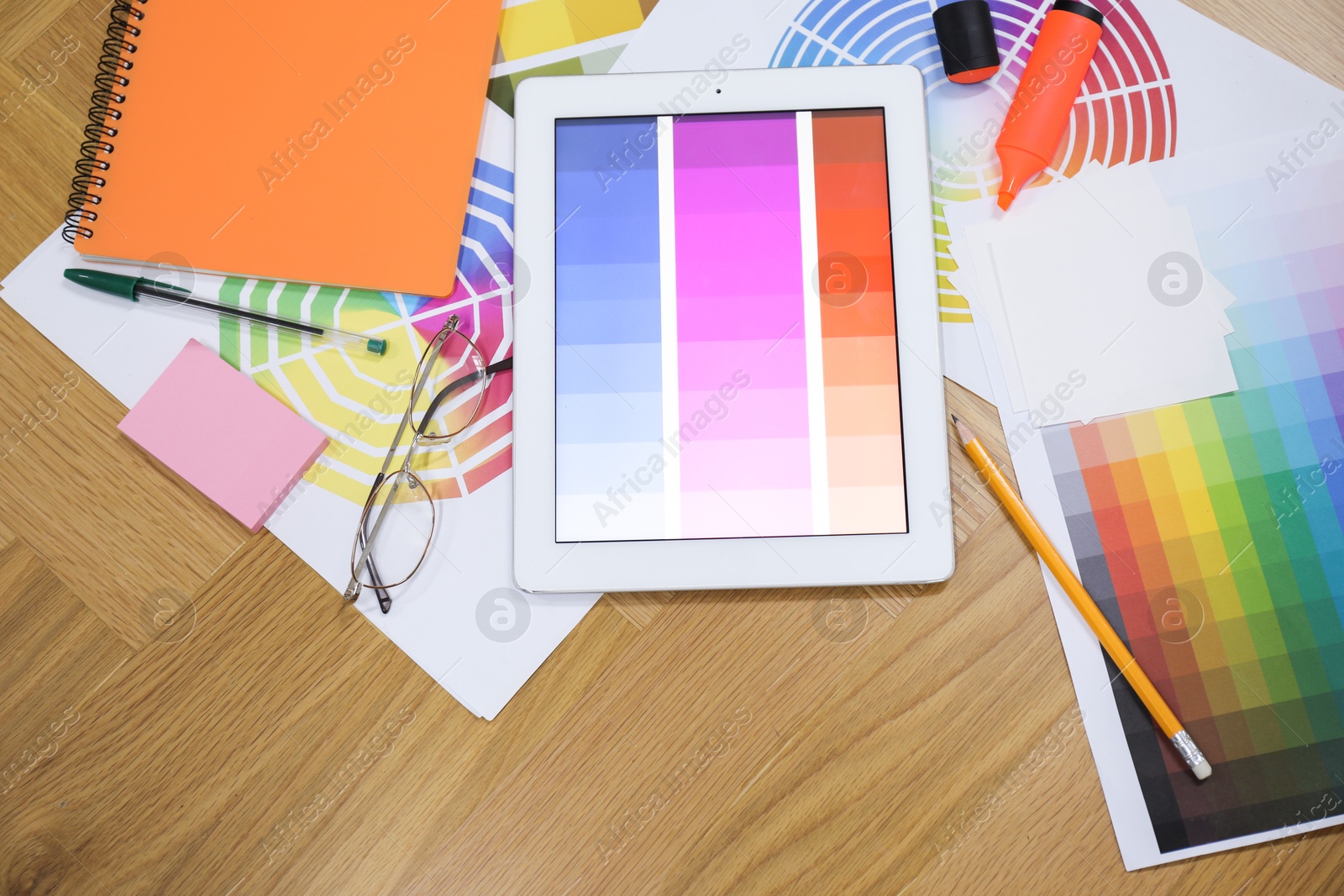 Photo of Designer's workplace with tablet, palettes and stationery on wooden table, flat lay