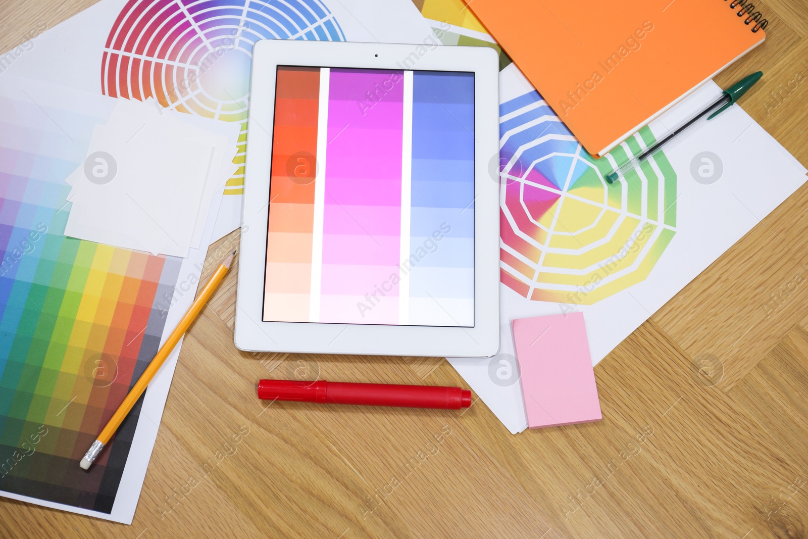 Photo of Designer's workplace with tablet, palettes and stationery on wooden table, flat lay