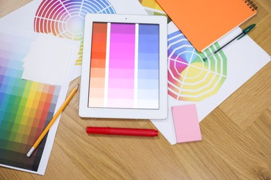 Photo of Designer's workplace with tablet, palettes and stationery on wooden table, flat lay