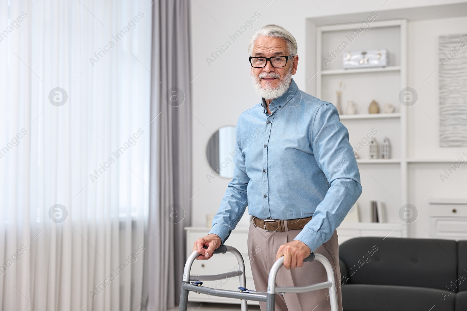 Photo of Senior man using walking frame at home. Space for text