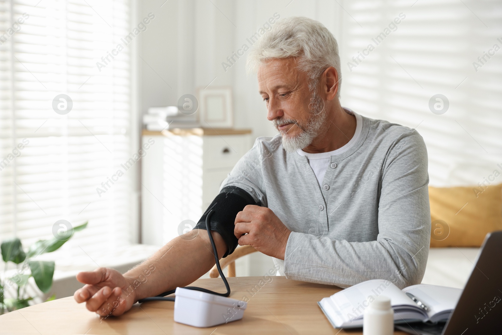 Photo of Senior man measuring blood pressure at wooden table indoors