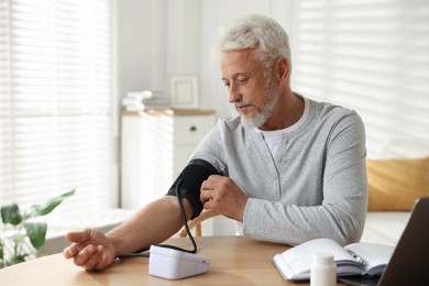 Photo of Senior man measuring blood pressure at wooden table indoors