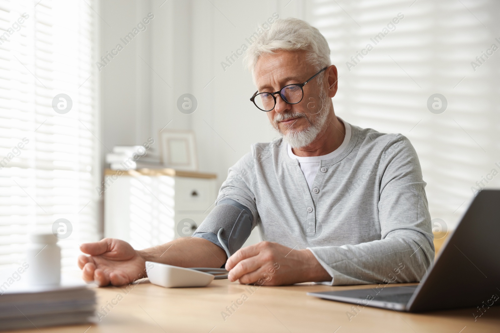 Photo of Senior man measuring blood pressure at table indoors