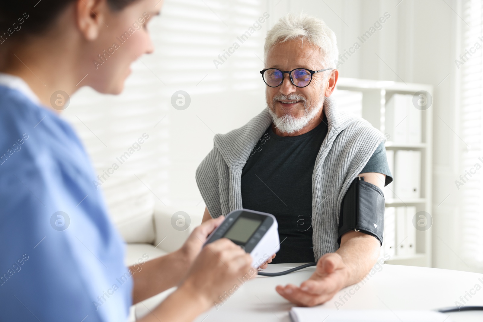 Photo of Doctor measuring patient's blood pressure at table indoors