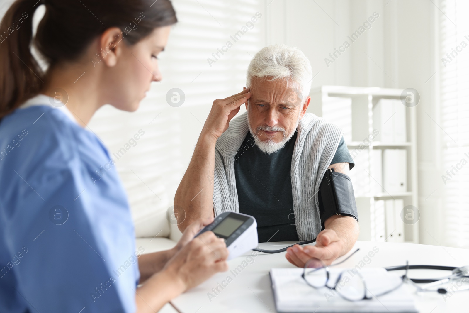 Photo of Doctor measuring patient's blood pressure at table indoors