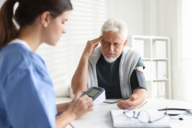 Photo of Doctor measuring patient's blood pressure at table indoors