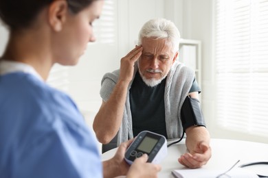 Photo of Doctor measuring patient's blood pressure at table indoors