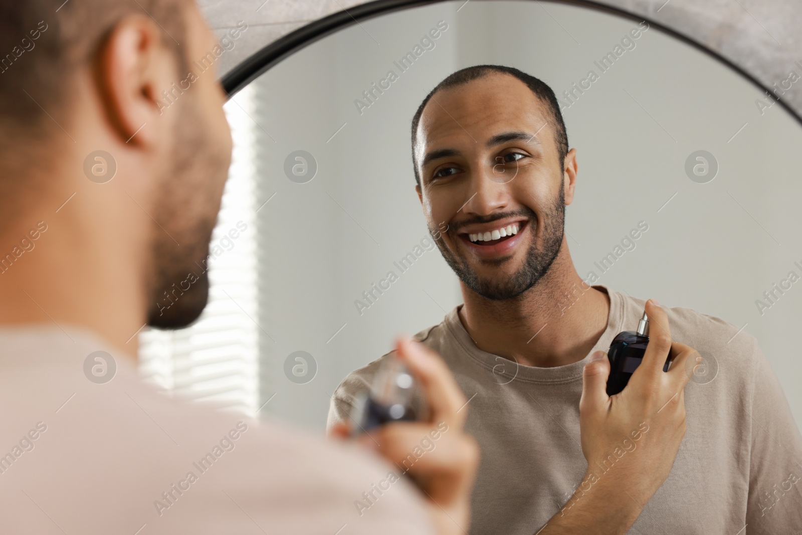 Photo of Smiling man spraying perfume near mirror in bathroom