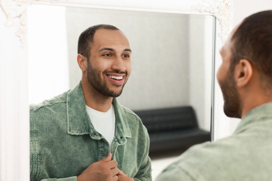 Photo of Smiling man dressing near mirror at home