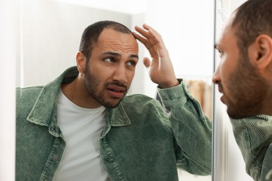 Photo of Worried man looking at mirror at home