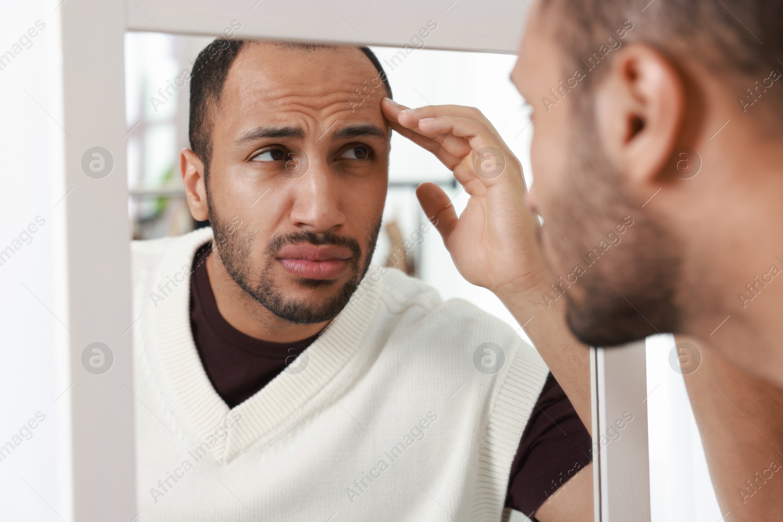 Photo of Worried man looking at mirror at home