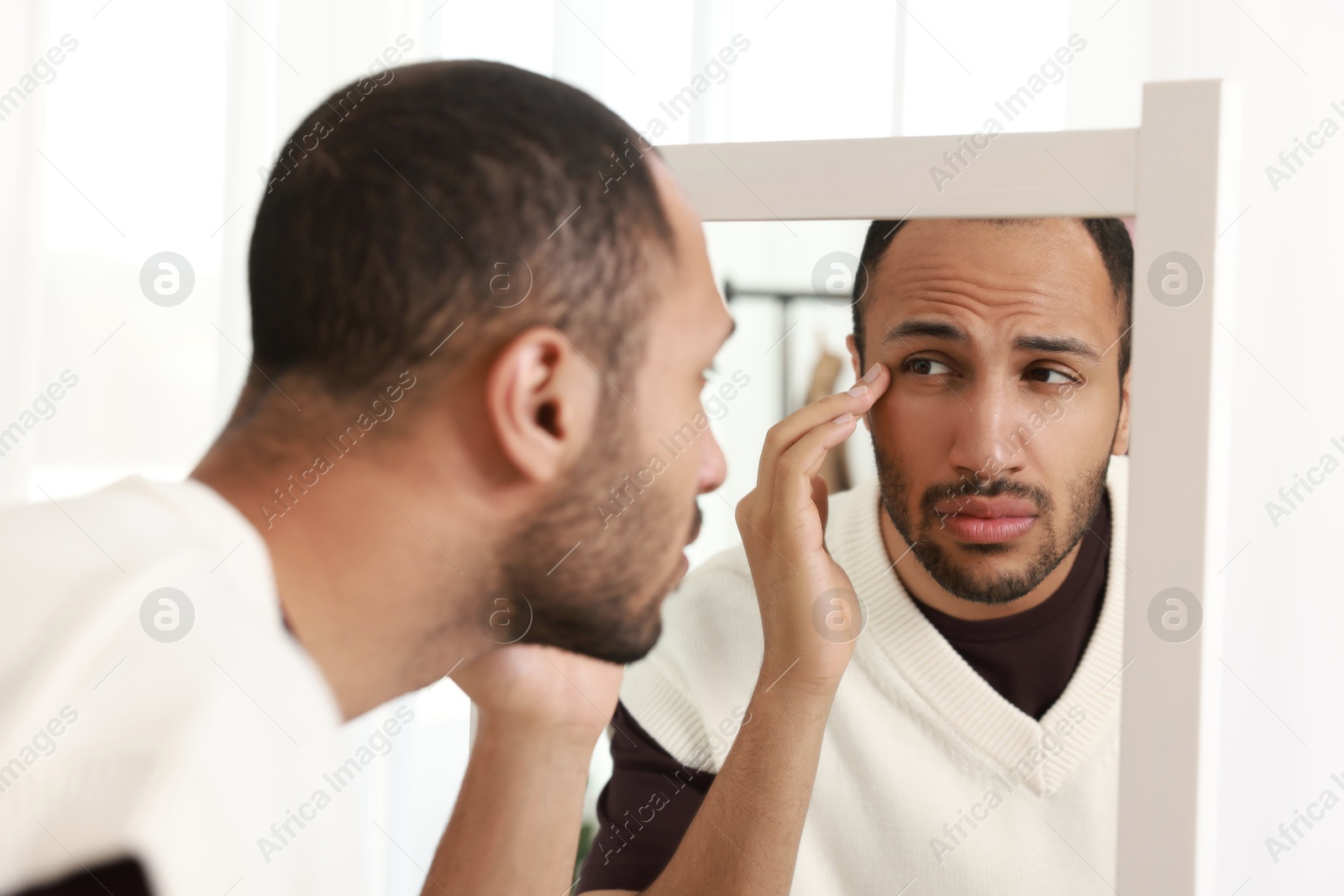 Photo of Worried man looking at mirror at home