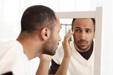 Worried man looking at mirror at home