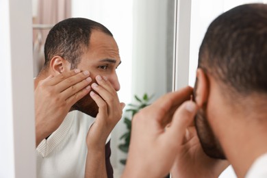 Photo of Worried man looking at mirror at home