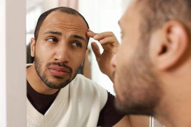 Worried man looking at mirror at home