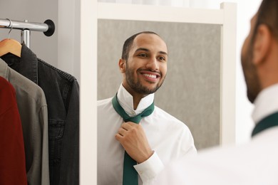 Photo of Smiling man adjusting necktie near mirror at home