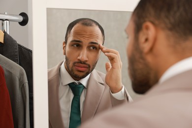 Photo of Worried man looking at mirror at home