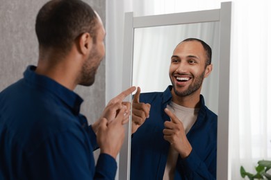 Photo of Smiling man looking at mirror at home