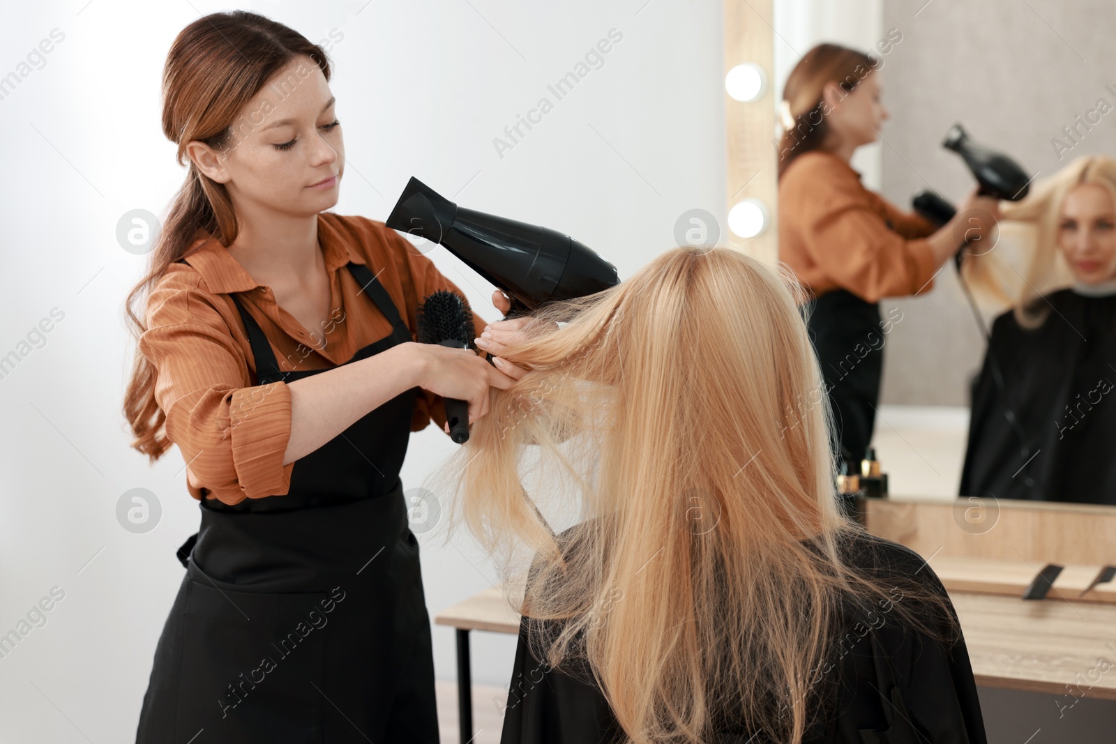 Photo of Hairdresser blow drying client's hair in salon