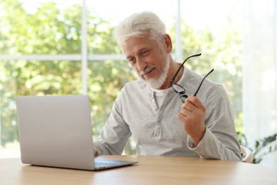 Photo of Senior man with glasses using laptop at table indoors