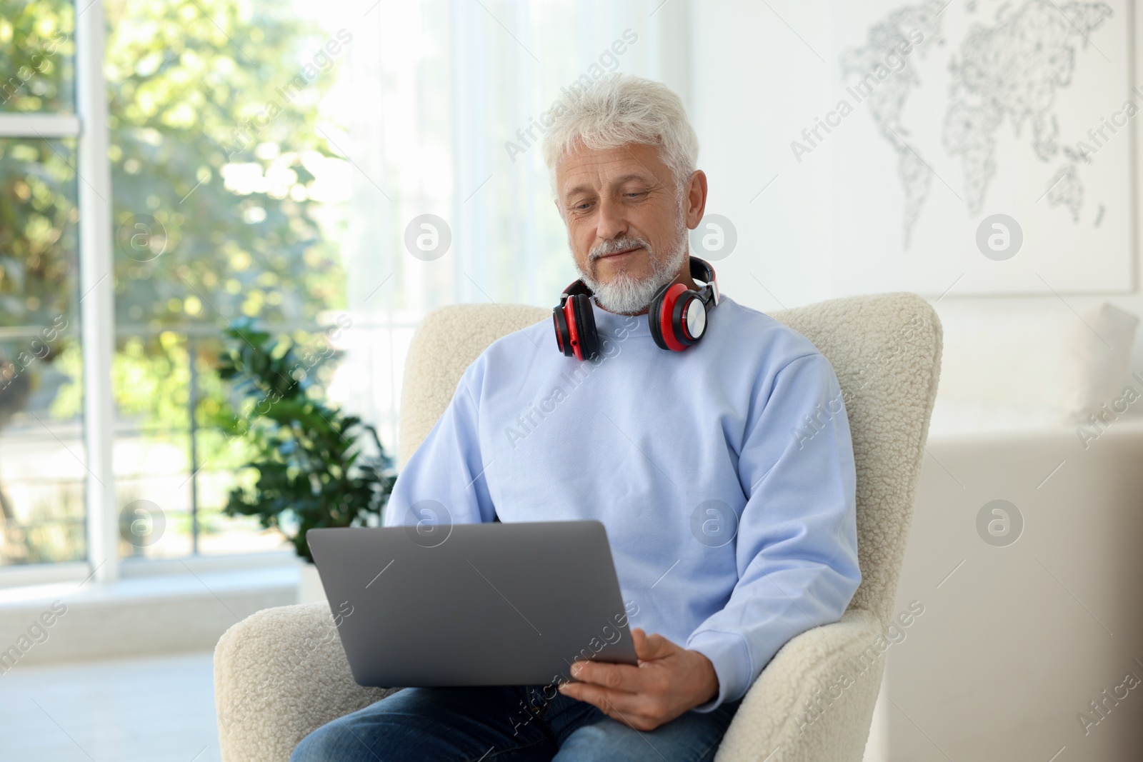 Photo of Senior man with headphones using laptop at home