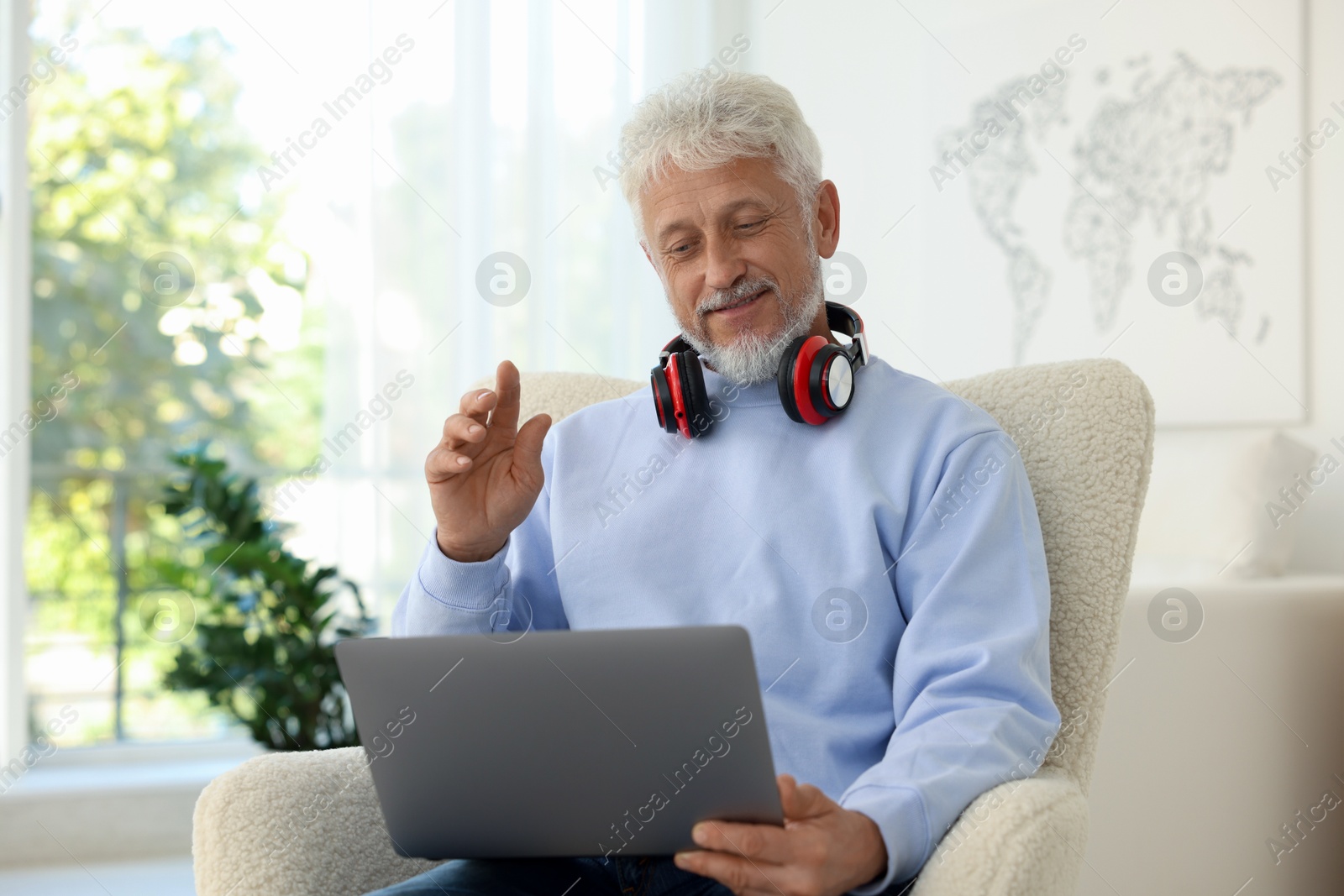 Photo of Senior man with headphones having video call via laptop at home