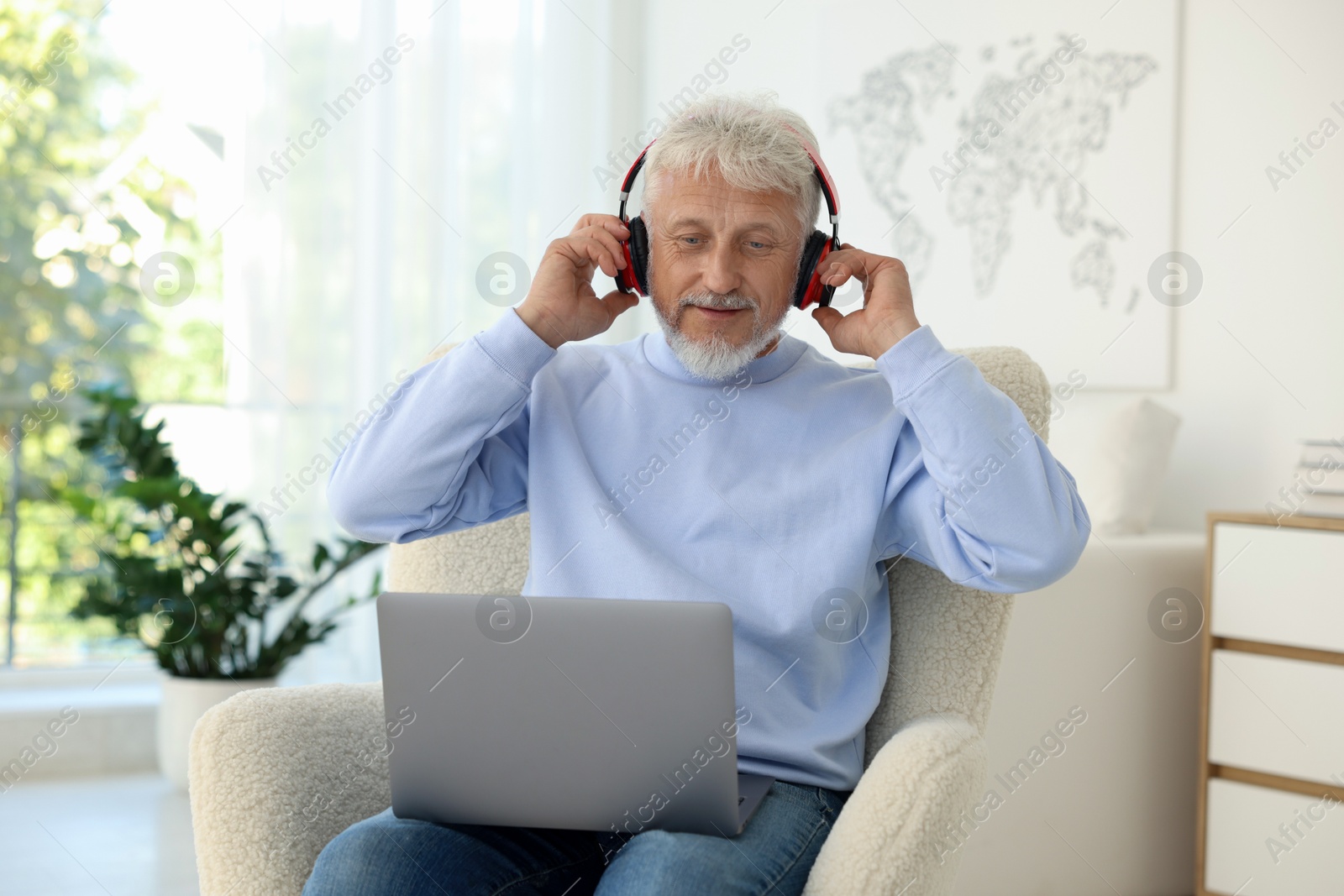 Photo of Senior man in headphones using laptop at home