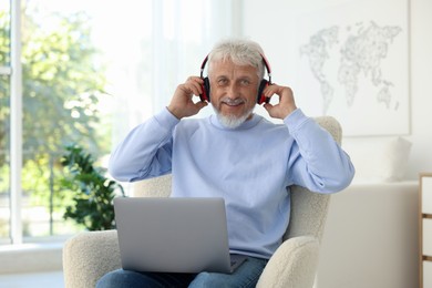 Photo of Senior man in headphones using laptop at home