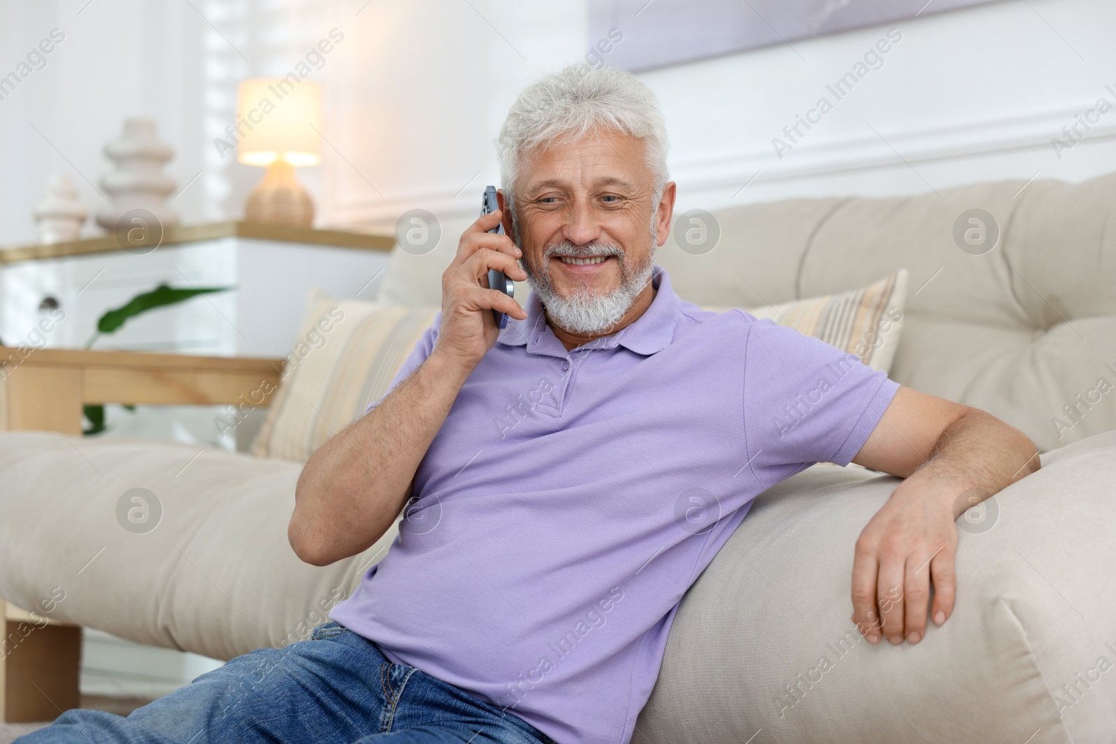 Photo of Smiling senior man talking on phone at home