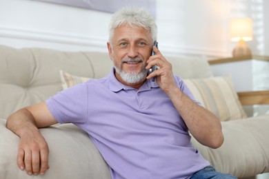 Photo of Smiling senior man talking on phone at home