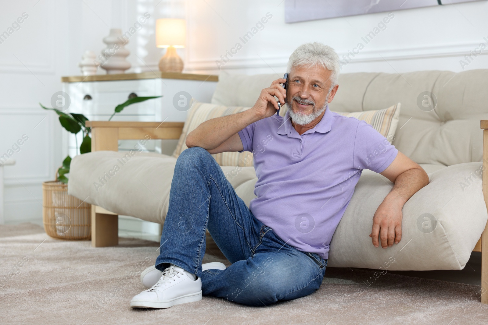 Photo of Smiling senior man talking on phone at home