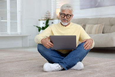 Photo of Senior man using laptop on floor at home