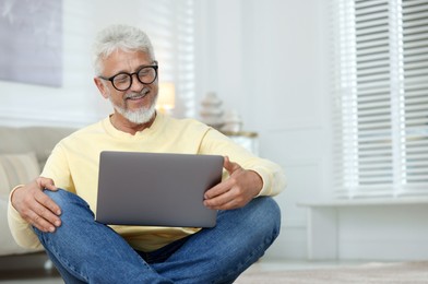 Photo of Senior man using laptop on floor at home, space for text