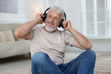 Photo of Smiling senior man in headphones listening to music at home