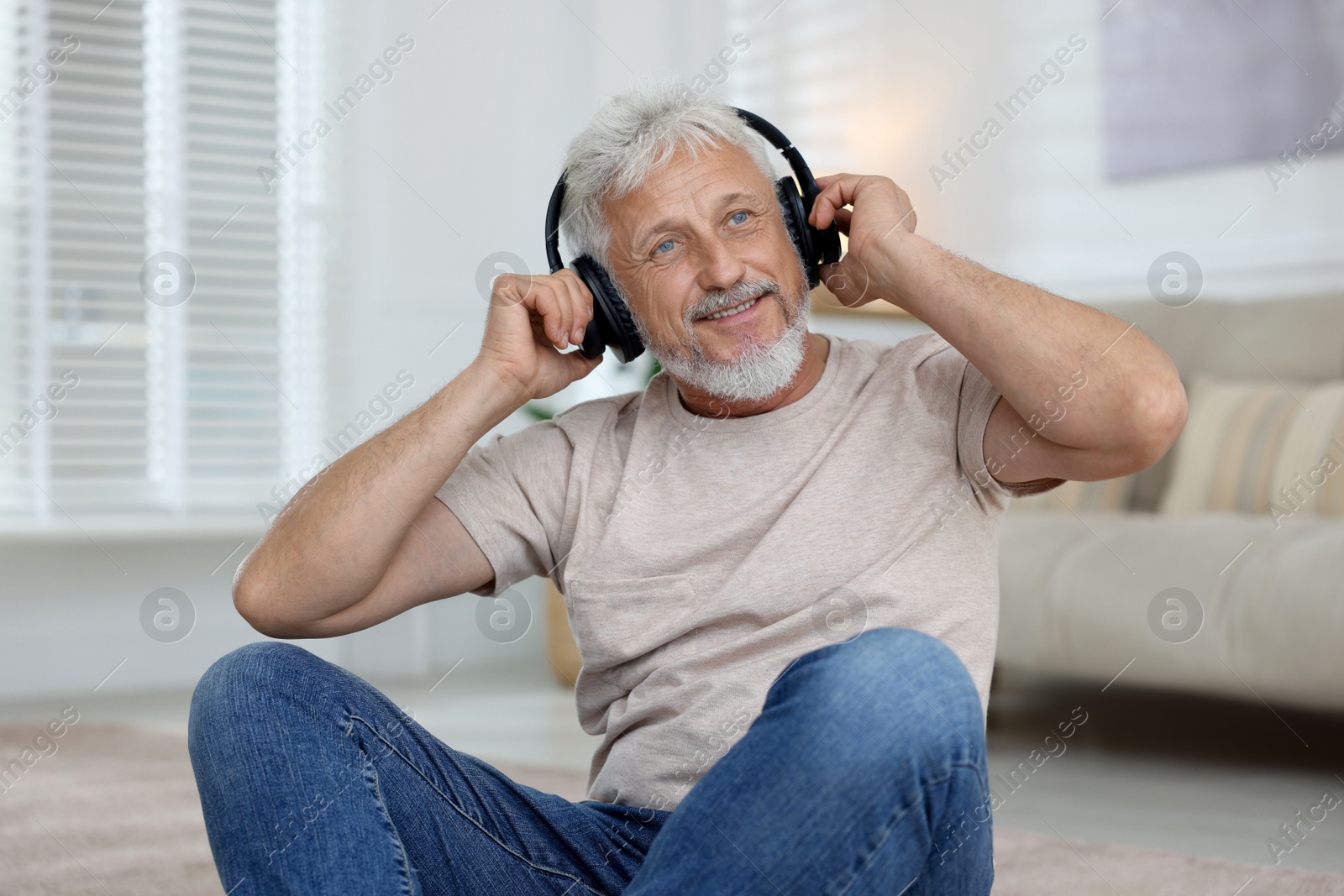 Photo of Smiling senior man in headphones listening to music at home