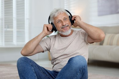 Smiling senior man in headphones listening to music at home