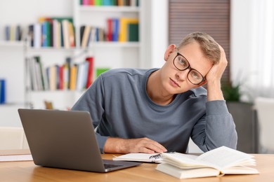 Photo of Preparing for exam. Student with laptop and book at table indoors