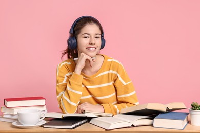 Photo of Preparing for exam. Student with books at table against pink background